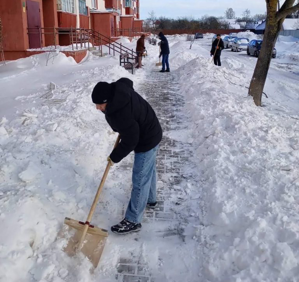 молодой человек в черной куртке чистит снег